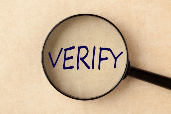Magnifying glass highlighting the word verify on paper.