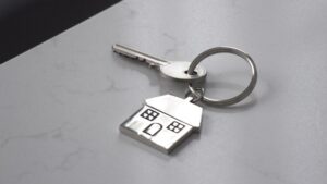 Silver house-shaped keychain with key on countertop.