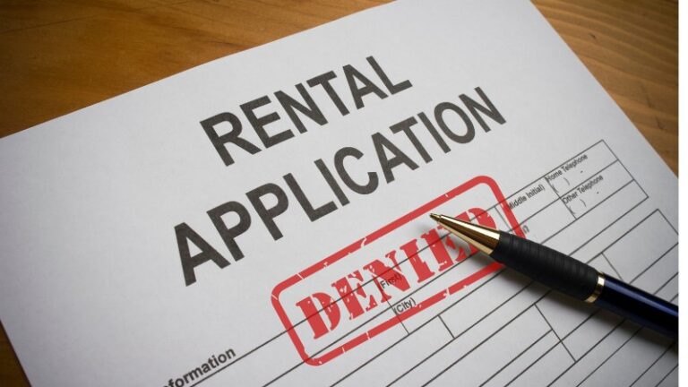 Rental application form with denied stamp and pen on desk.