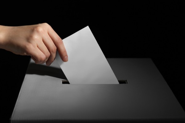 Hand placing ballot into slot of box.