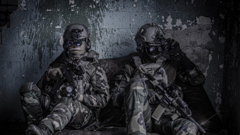 Two soldiers in tactical gear with rifles indoors