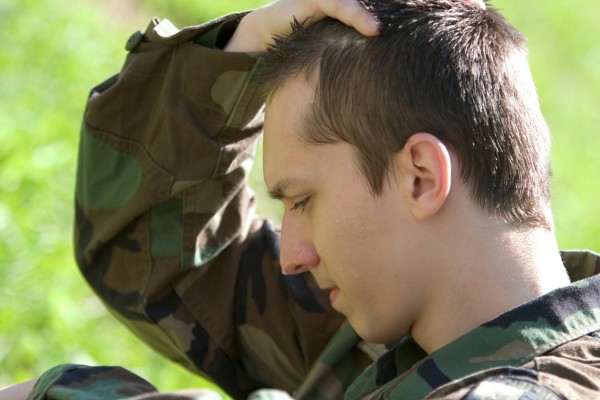 Tired soldier in uniform holding head with hand