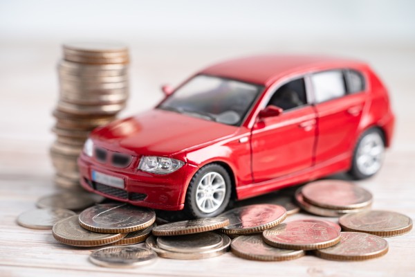 Red toy car surrounded by stacked and scattered coins.