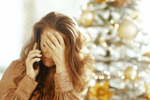 A distressed woman covers her face with one hand while talking on the phone, showing emotional stress or frustration.